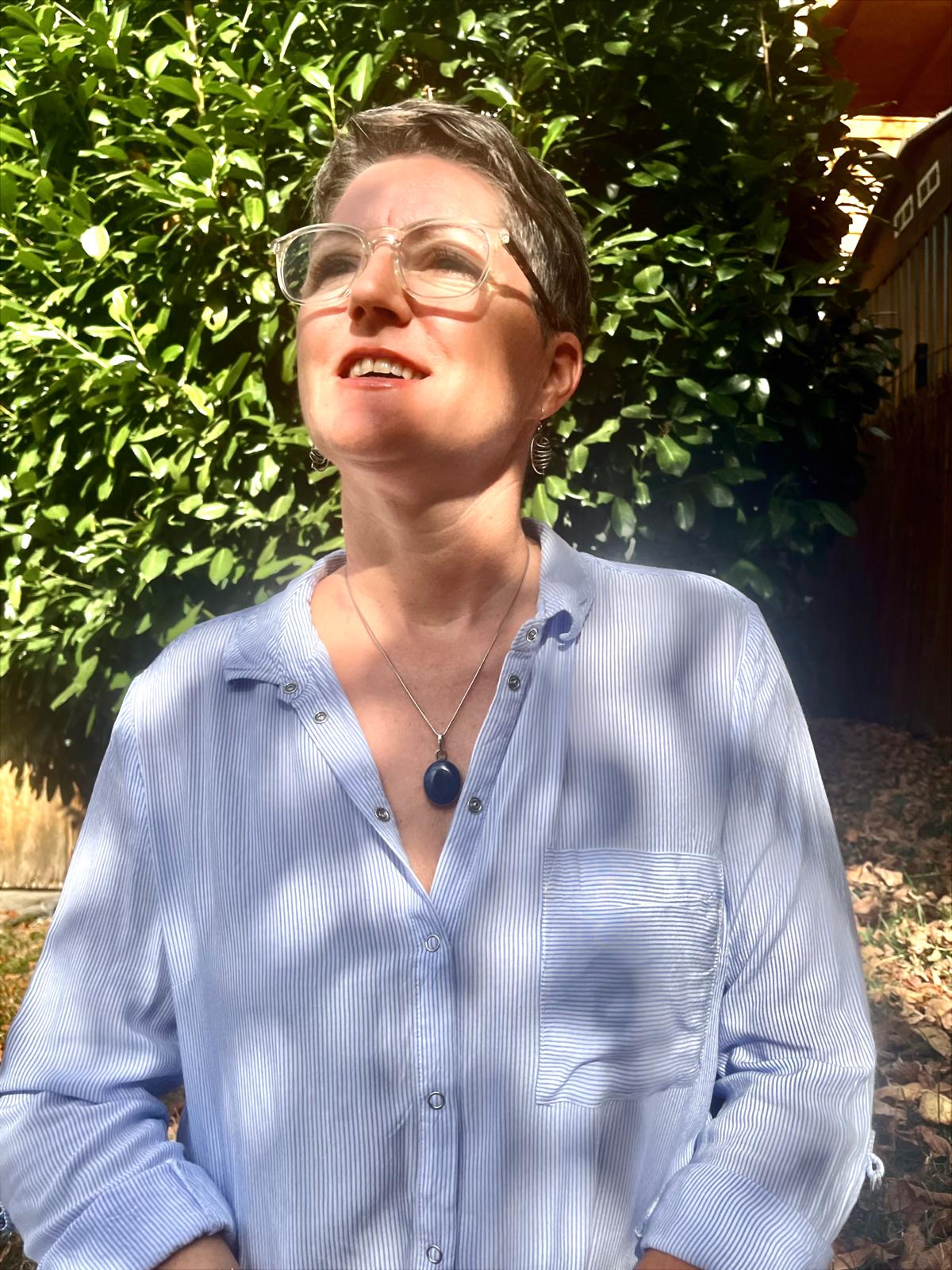 Michaela Seiß, zertifizierte Breathwork-Trainerin, im Sonnenlicht vor grünen Blättern